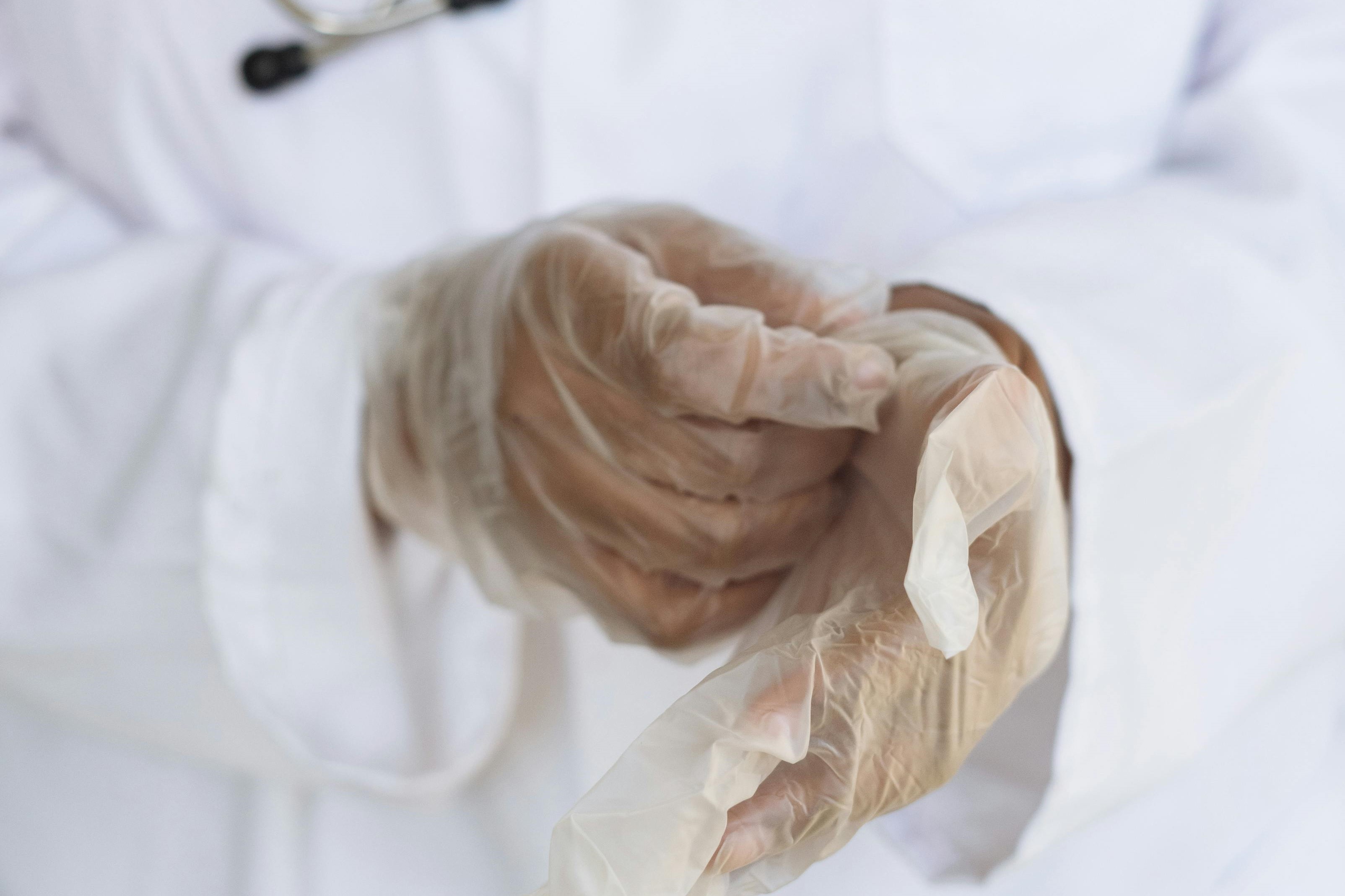A doctor in a white coat puts on semi-opaque white gloves.